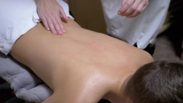 Les mains du masseur massent le dos d'un adolescent, un enfant dans un salon de spa — Video