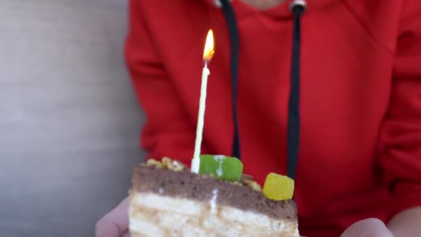 Una mujer sostiene un plato con un pedazo de pastel de cumpleaños y una vela encendida. 4K — Vídeo de stock