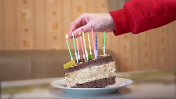 Naispuolinen käsi sytyttää kynttilöitä syntymäpäiväkakun palalla. Hidastus — kuvapankkivideo