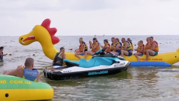 Heureux touristes en gilets de sauvetage assis sur une banane gonflable, dragon en pleine mer — Video
