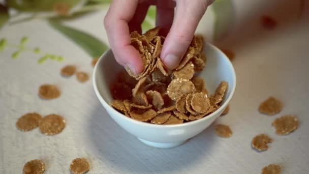 Female Hand Scatters, Pours Out, Throws Corn Flakes into a White Bowl. Close up — Stock Video