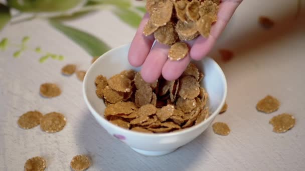 Female Hand Scatters, Pours Out, Throws Corn Flakes into a White Bowl. Close up — Stock Video