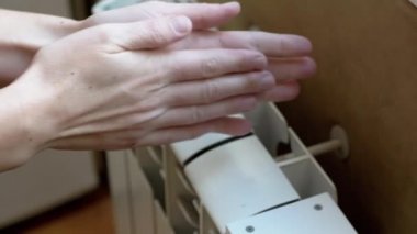 A Woman Warms Hands on a Battery at Home in a Room. 4K. Close up. Slow motion