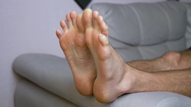Un homme pétrit, fait de la gymnastique des orteils, allongé sur le canapé. 4K. Gros plan — Video