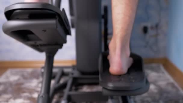 Босоногий мужчина педалирует ногами на тренажере Elliptical Cross Simulator дома. 4K — стоковое видео