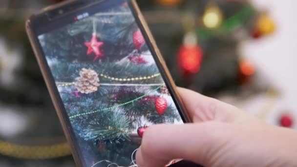 Kvinnliga händer är att skjuta en video av julgranen på en smartphone. Närbild — Stockvideo