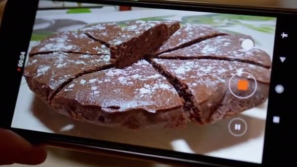 Weibliche Hände filmen mit einem Smartphone einen Schokoladenkuchen in der Küche. 4K — Stockvideo