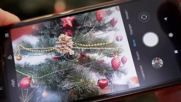 Manos femeninas tomando una foto del árbol de Navidad en un teléfono inteligente. 4K. De cerca. — Vídeos de Stock