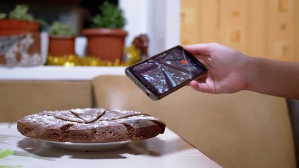 Manos femeninas filma video de un pastel de chocolate en la cocina en un teléfono inteligente. 4K — Vídeos de Stock