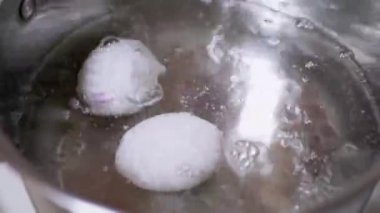 İki yumurta kaynayan bir tencerede kaynıyor. Yavaş çekim. Yakın plan.