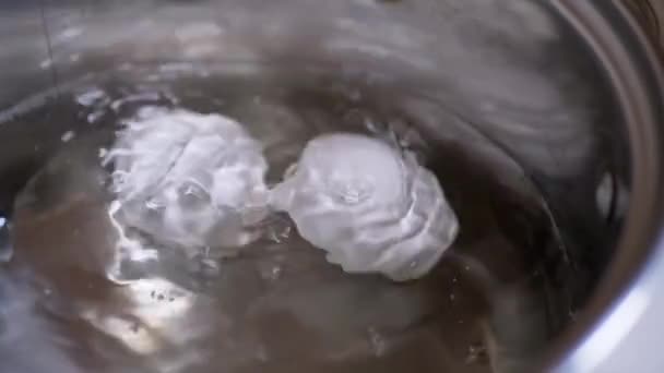 Due uova stanno bollendo in una pentola di acqua bollente. Al rallentatore. Primo piano — Video Stock