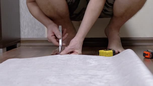 Hombre, Sentado en el suelo, corta una tira de papel pintado para pegar con un cuchillo — Vídeos de Stock