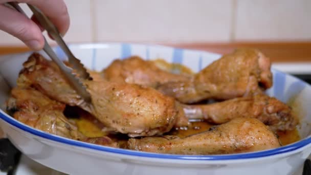 Uma mulher coloca as pernas de frango suculentas cozidas em uma forma resistente ao calor com pinças. 4K — Vídeo de Stock