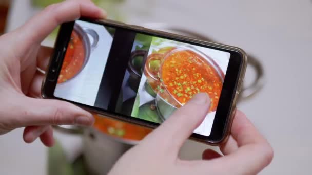 Een vrouw kijkt foto van traditionele Oekraïense rode Borscht in een smartphone — Stockvideo