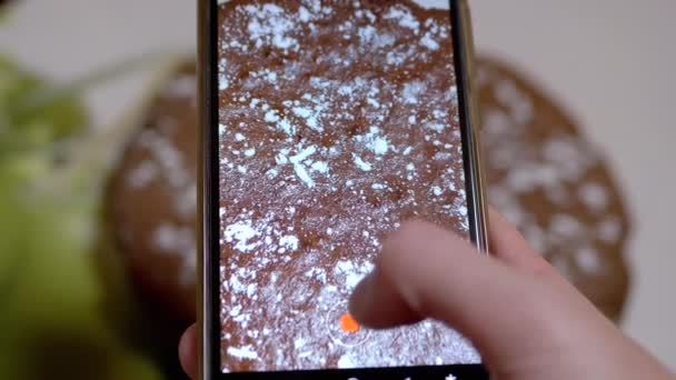Manos femeninas filma video de un pastel de chocolate en la cocina en un teléfono inteligente. 4K — Vídeos de Stock