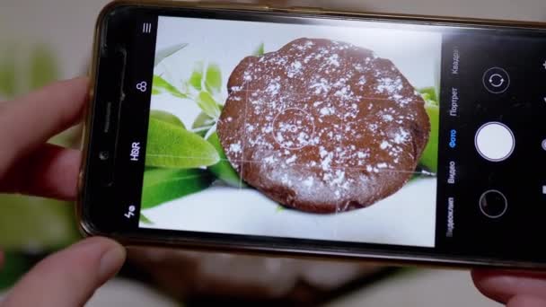 Weibliche Hände fotografieren einen Schokoladenkuchen in der Küche mit einem Smartphone. 4K — Stockvideo