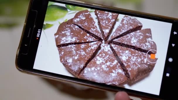 As mãos femininas filmam vídeo de uma torta de chocolate na cozinha em um telefone inteligente. 4K — Vídeo de Stock