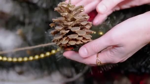 Vrouwelijke handen hangen een grote bruine kegel aan de kerstboom. Zoom uit. Sluiten. — Stockvideo