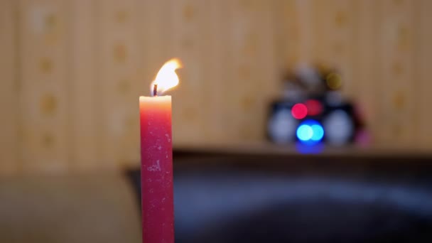 Vela roja ardiente con una llama brillante en movimiento sobre un fondo borroso de luces — Vídeo de stock