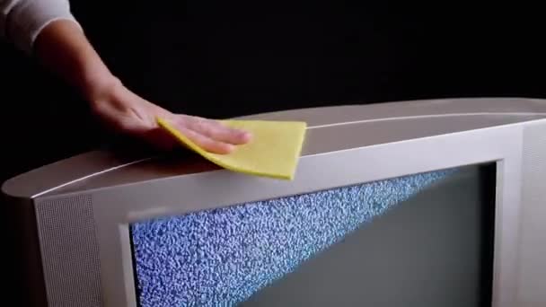 Weibliche Hand wischt Staub mit einem gelben Lappen von der Oberfläche eines alten Fernsehers im dunklen Raum — Stockvideo