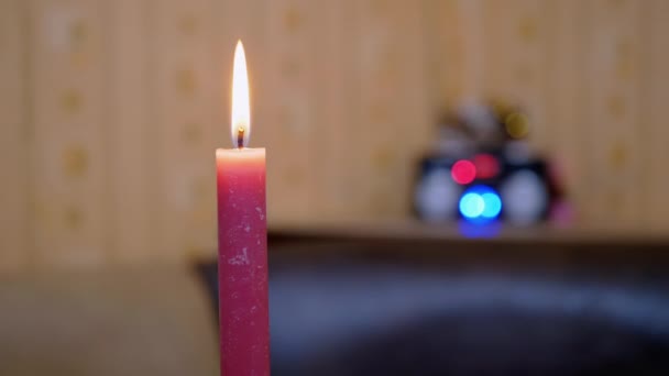 Vela roja ardiente con una llama brillante en movimiento sobre un fondo borroso de luces — Vídeo de stock