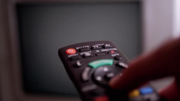 Ένα αρσενικό χέρι κατέχει ένα τηλεχειριστήριο και διακόπτες που τρεμοπαίζουν κανάλια στην οθόνη — Αρχείο Βίντεο