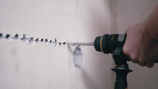 Um construtor usando um perfurador faz um furo em uma parede de concreto para instalar uma tomada — Vídeo de Stock