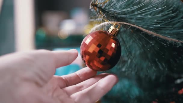 Uma mão feminina gira uma bola de Natal vermelha brilhante pendurada em uma árvore de Natal — Vídeo de Stock