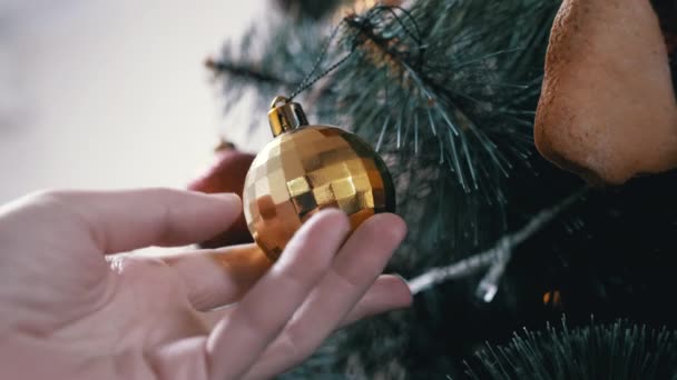 Ένα γυναικείο χέρι περιστρέφεται μια λαμπερή κίτρινη χριστουγεννιάτικη μπάλα κρέμεται σε ένα χριστουγεννιάτικο δέντρο — Αρχείο Βίντεο