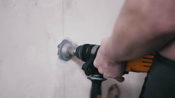 Budowniczy za pomocą wykrawacza robi dziurę w betonowym murze, aby ustawić gniazdo zasilania — Wideo stockowe