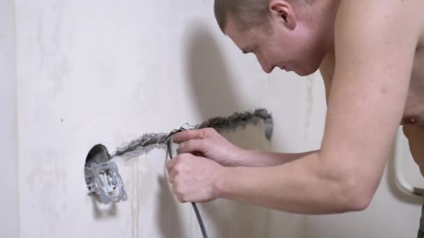 Homme électricien pose un câble isolant dans le mur pour installer une prise. 4K — Video