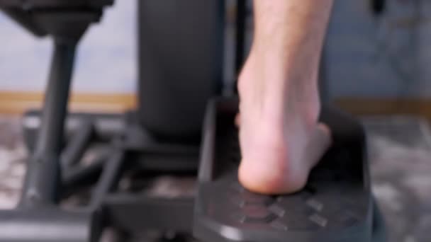 Босоногий мужчина педалирует ногами на тренажере Elliptical Cross Simulator дома. Zoom — стоковое видео