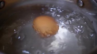 Yumurta bir tencere kaynar suda kaynatılır. Yavaş çekim. Yakın plan.