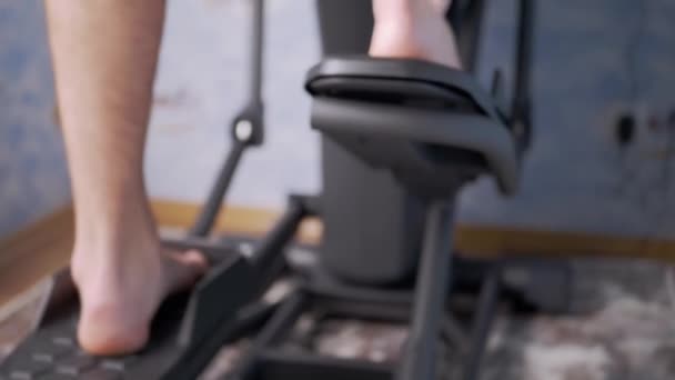 Босоногий мужчина педалирование ног на эллиптический кросс тренер симулятор дома — стоковое видео