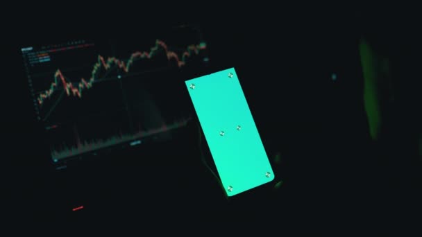 Een handelaar houdt een smartphone met een groen scherm in handen in een donkere kamer. 4K — Stockvideo