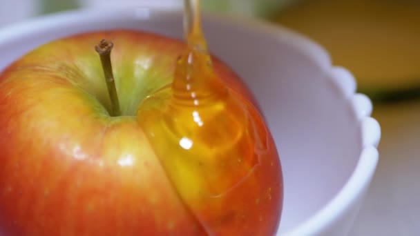Žlutý průsvitný hojící med nalévá v potoce na Zralé červené jablko v misce — Stock video