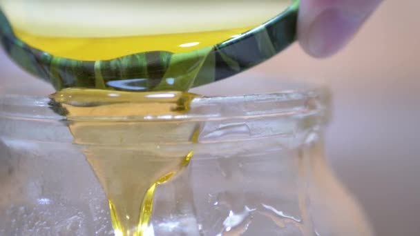 Ένα γυναικείο χέρι χύνει χρυσό κίτρινο διαφανές μέλι από ένα καπάκι σε ένα γυάλινο βάζο — Αρχείο Βίντεο
