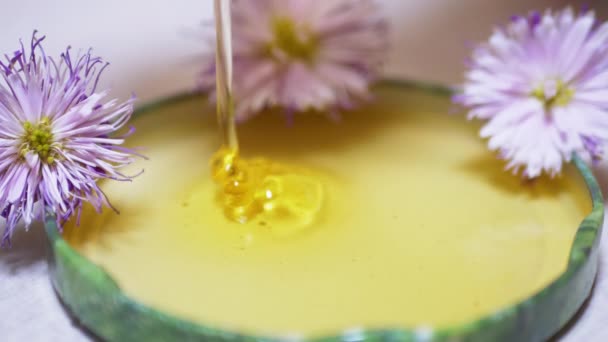 La miel natural transparente fluye en una corriente delgada hacia una tapa, un tazón. De cerca. — Vídeos de Stock