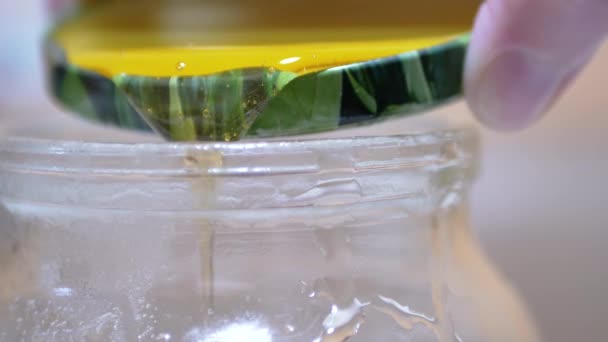 A női kéz arany sárga átlátszó mézet önt a fedeléről egy üvegedénybe. — Stock videók
