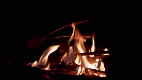 Мужские руки жарят две сочные колбасы ночью на костре в лесу — стоковое видео