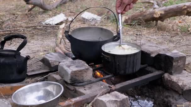 Mannelijke bereiding van voedsel in een pan op een vreugdevuur in bossen buiten. 4K. Sluiten. — Stockvideo