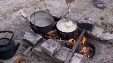 Açık havada, Ormanda Şenlik Ateşi 'nde bir tencerede yemek hazırlayan bir erkek. 4 bin. Kapat.