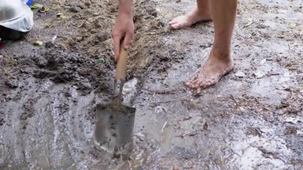 Человек копает штормовой сток, траншею, дренаж во влажной земле с помощью лопаты — стоковое видео