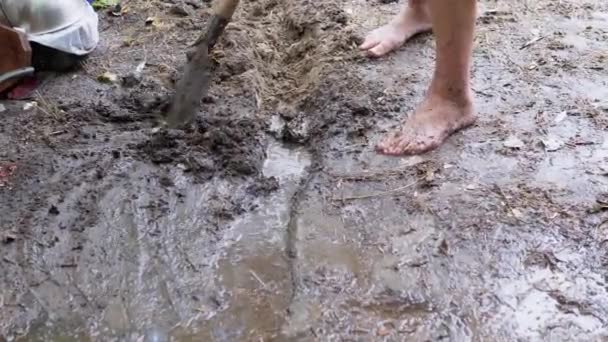 Человек копает штормовой сток, траншею, дренаж во влажной земле с помощью лопаты — стоковое видео
