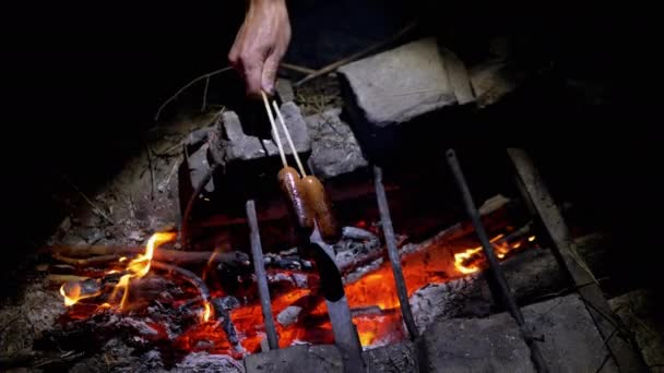 Hombre hambriento freír dos jugosas salchichas en la noche en una hoguera al aire libre en el bosque — Vídeo de stock