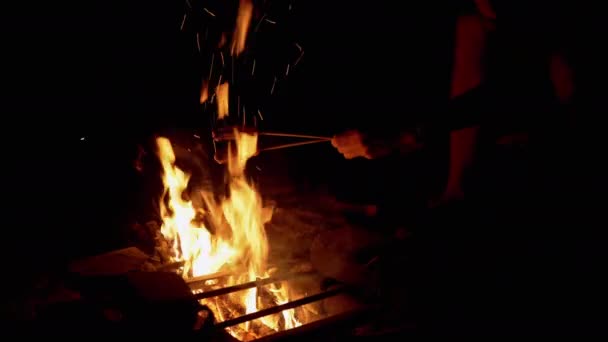 Hungriger Mann frittiert nachts zwei saftige Würste am Lagerfeuer im Freien im Wald — Stockvideo