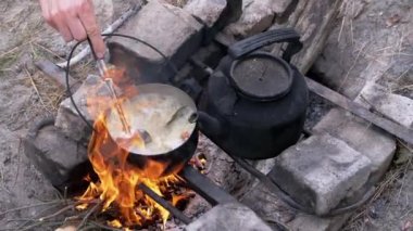 Açık havada, Ormanda Şenlik Ateşi 'nde bir tencerede yemek hazırlayan bir erkek. Yakınlaştır. Kapat.