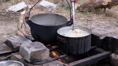 Açık havada, Ormanda Şenlik Ateşi 'nde bir tencerede yemek hazırlayan bir erkek. Yakınlaştır. Kapat.