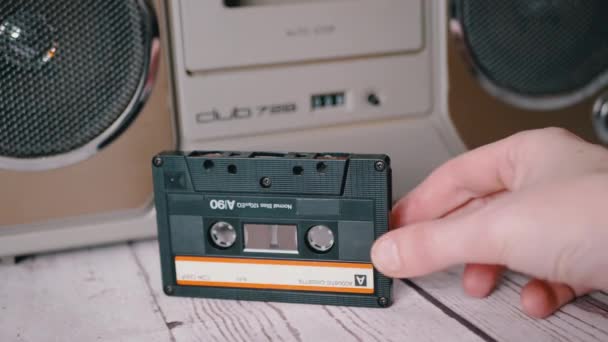 La mano femenina sostiene un casete de audio antiguo de los años 90 cerca de una grabadora de cinta estéreo — Vídeos de Stock