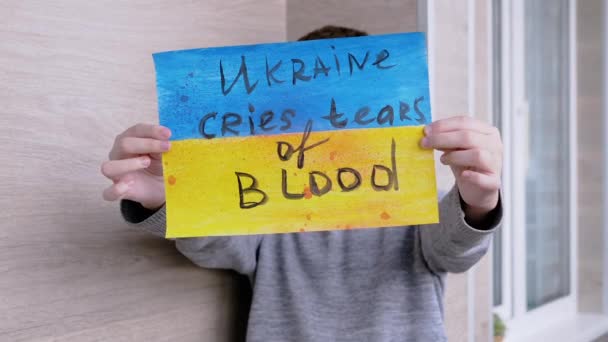 Niño sostiene una pancarta con una bandera azul y amarilla con texto sobre la guerra en Ucrania — Vídeos de Stock